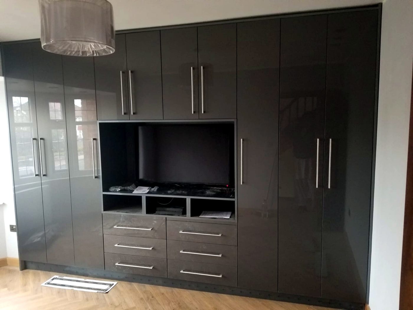Bespoke high-gloss grey fitted wardrobe with integrated TV media unit and drawers, installed by BFK