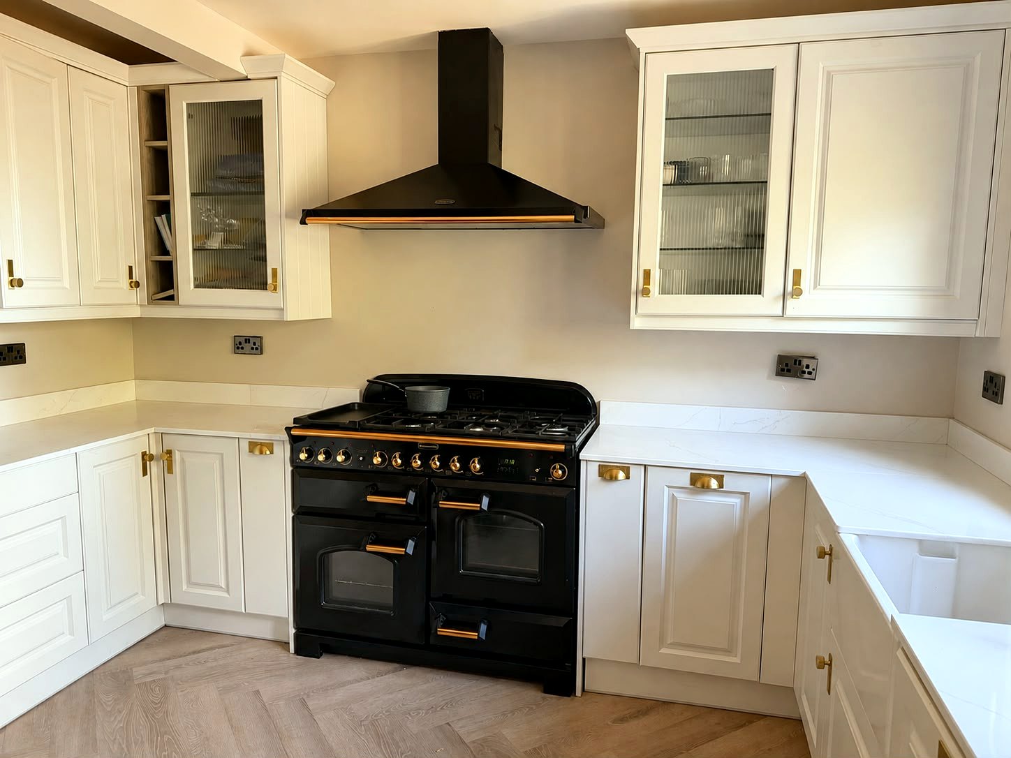 Cream in-frame kitchen with black range cooker, brass hardware, reeded glass cabinets and quartz worktops, installed by BFK