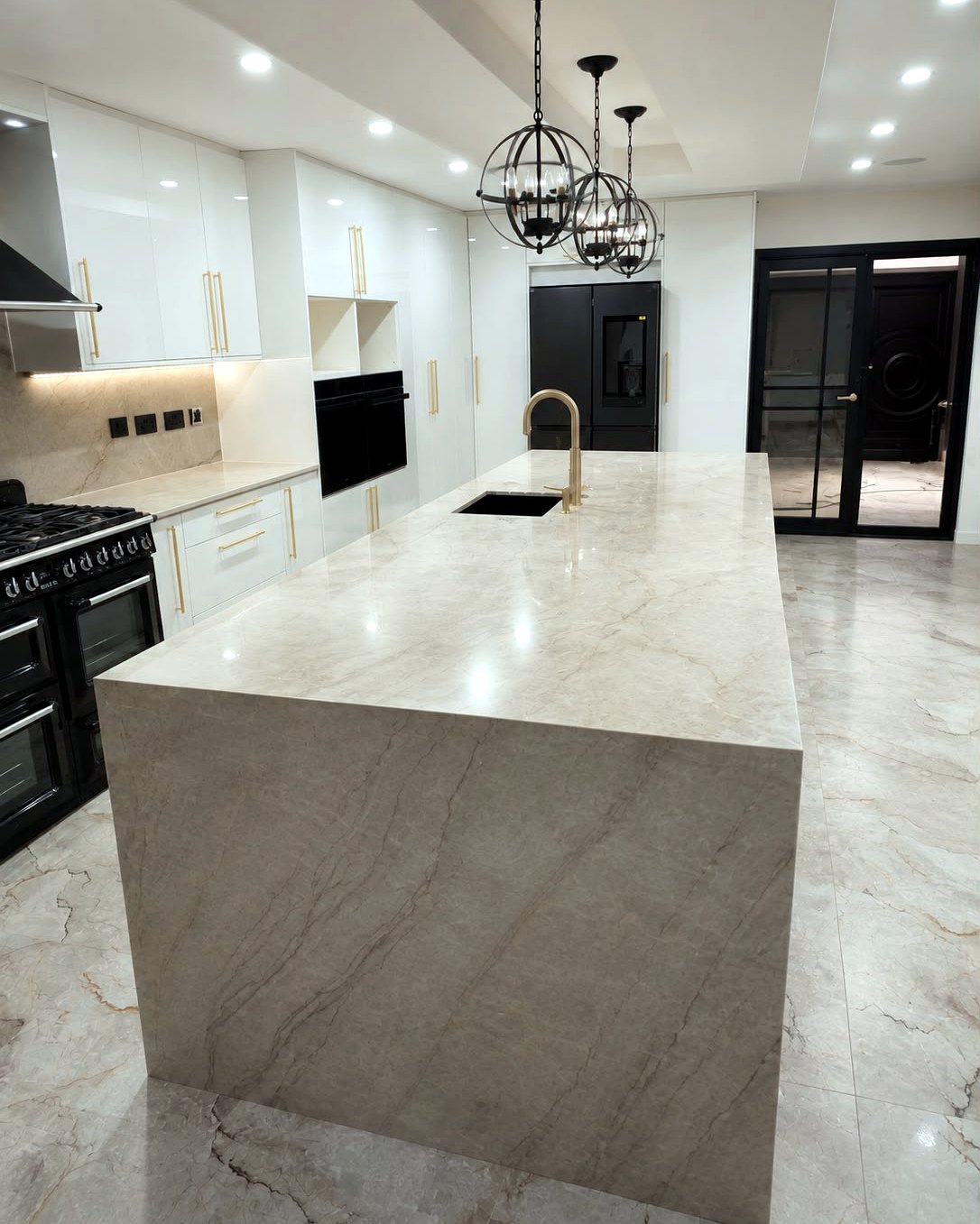 Gloss white kitchen with large quartzite waterfall island, brass handles and range cooker, installed by BFK
