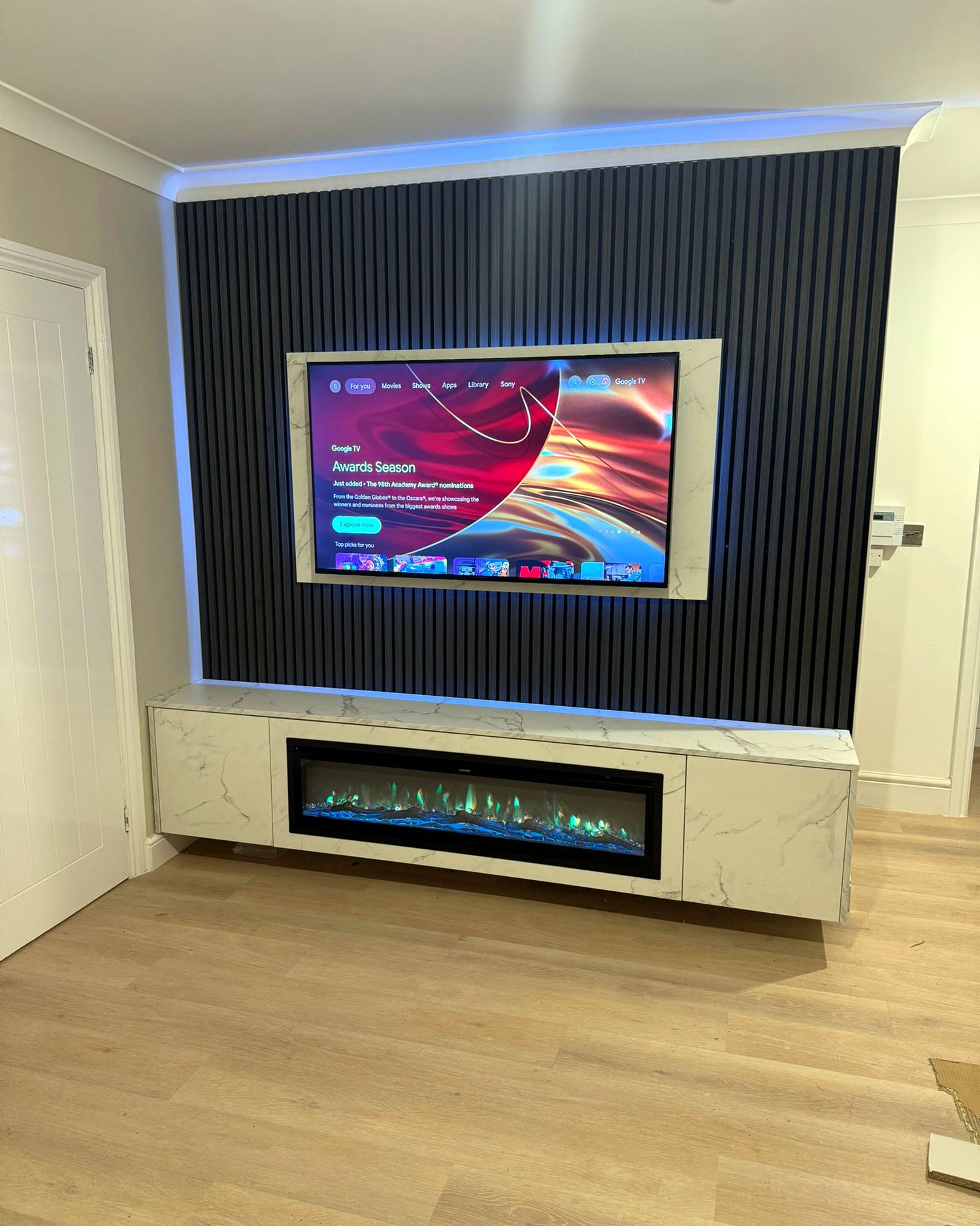 Bespoke media wall with black slatted acoustic panelling, recessed TV, marble-effect floating console and inset electric fire, installed by BFK